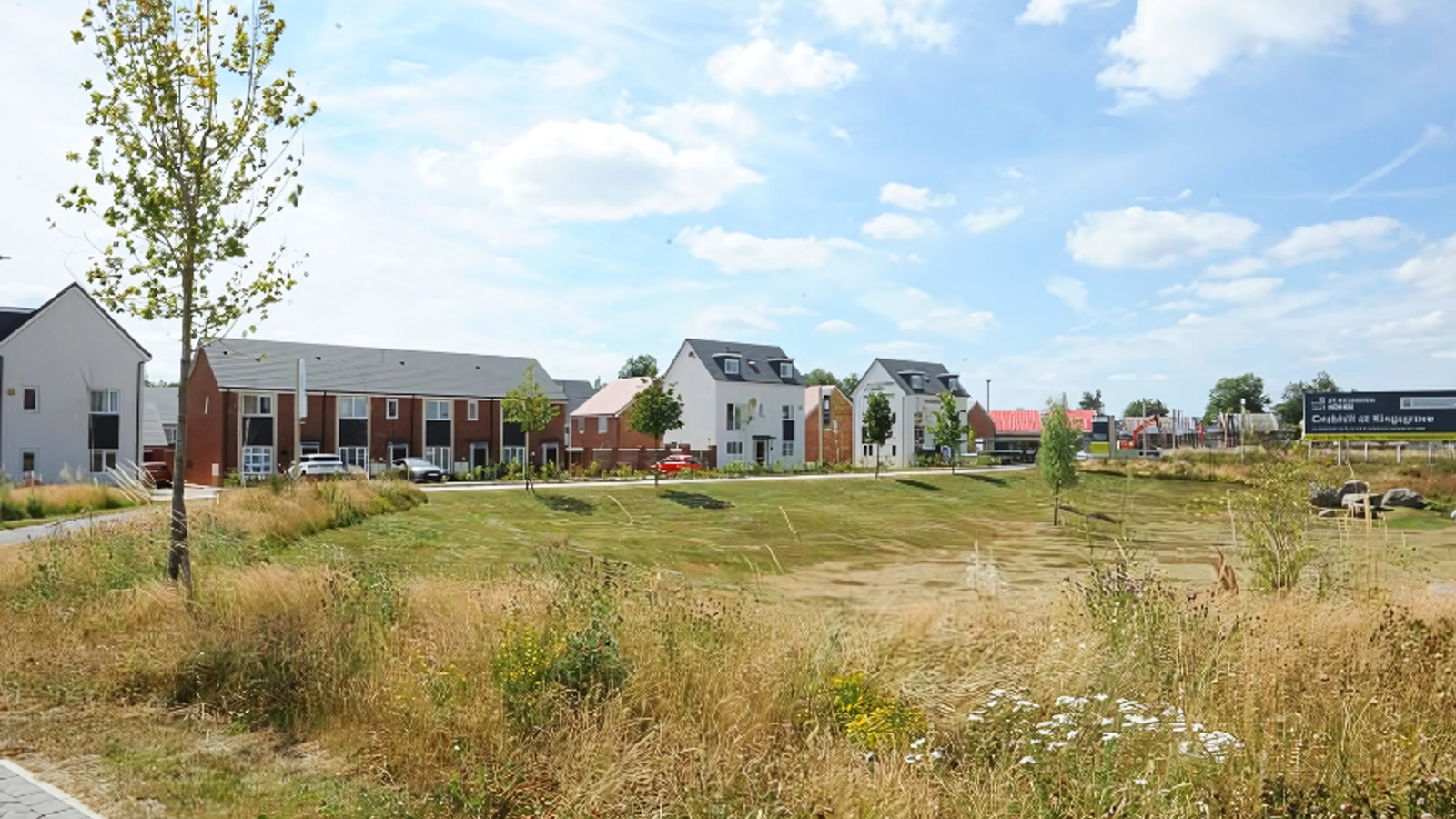 New residential housing development featuring modern homes, landscaped green spaces, and prominent marketing signage under a clear blue sk