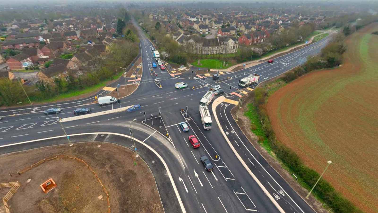 Aerial view of a major road intersection with multiple lanes, traffic lights, and surround residential and rural areas - Banbury Road, Bicester - Section 278