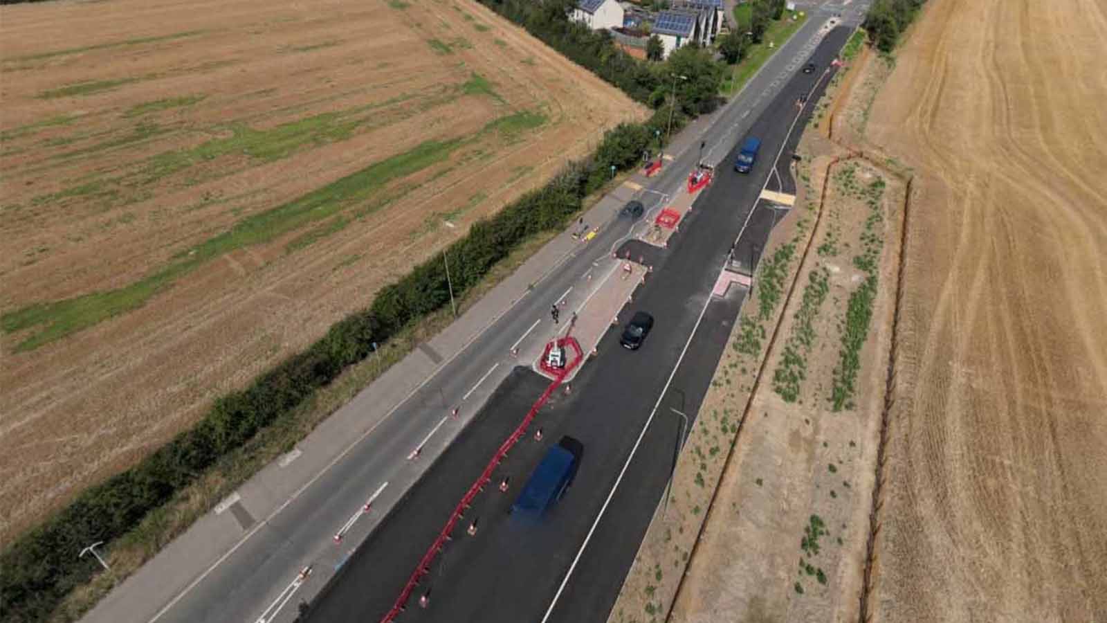 Aerial view of a rural road improvement project featuring newly laid asphalt, temporary traffic management barriers, and active vehicle lanes - Banbury Road, Bicester - Section 278