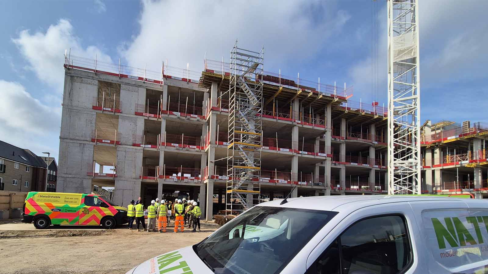 Construction workers in high-visibility gear gathered near a multi-storey care home building under construction.