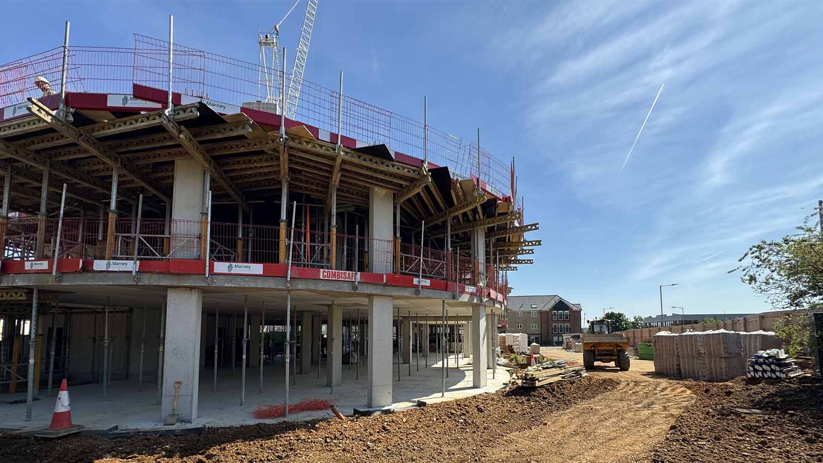 Curved concrete care home under construction with scaffolding, railings and site preparation materials around.