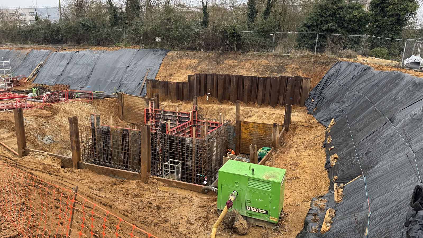Deep excavation site with foundation reinforcements, formwork, and a dewatering pump in use for a care home.
