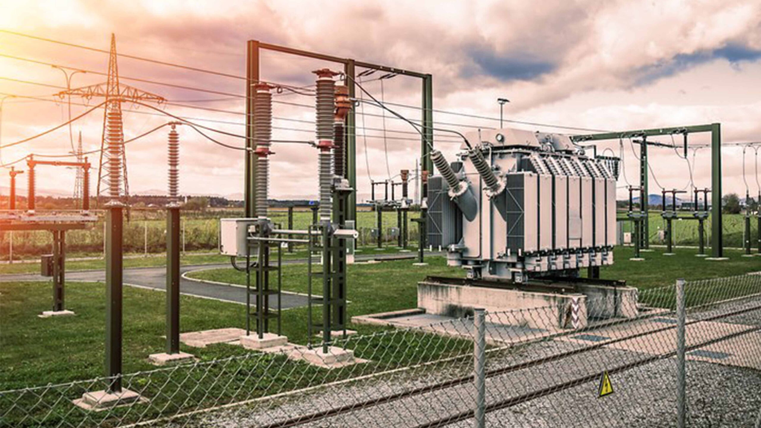 Solar PV Farm High-voltage electrical substation with transformers, power lines, and safety fencing under a cloudy sky.