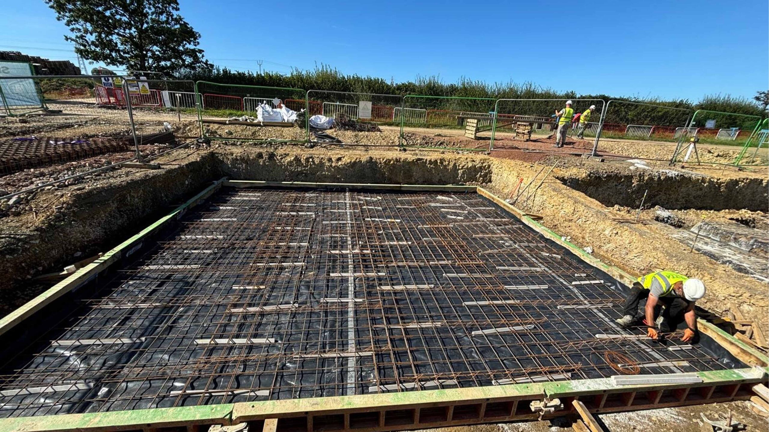 Solar PV Farm Construction worker securing steel reinforcement bars on a foundation slab framework at a building site, preparing for concrete pour