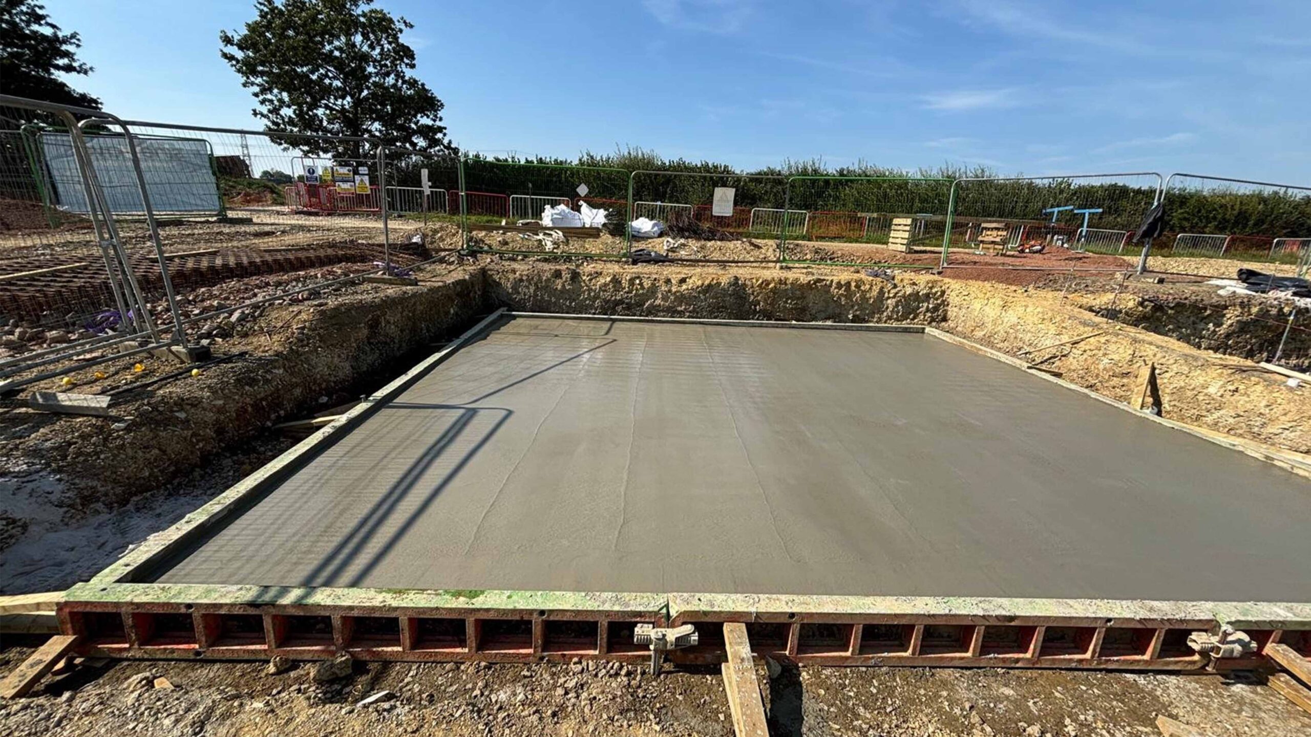 Solar PV Farm Freshly poured concrete foundation slab at a construction site, surrounded by safety fencing and excavation work