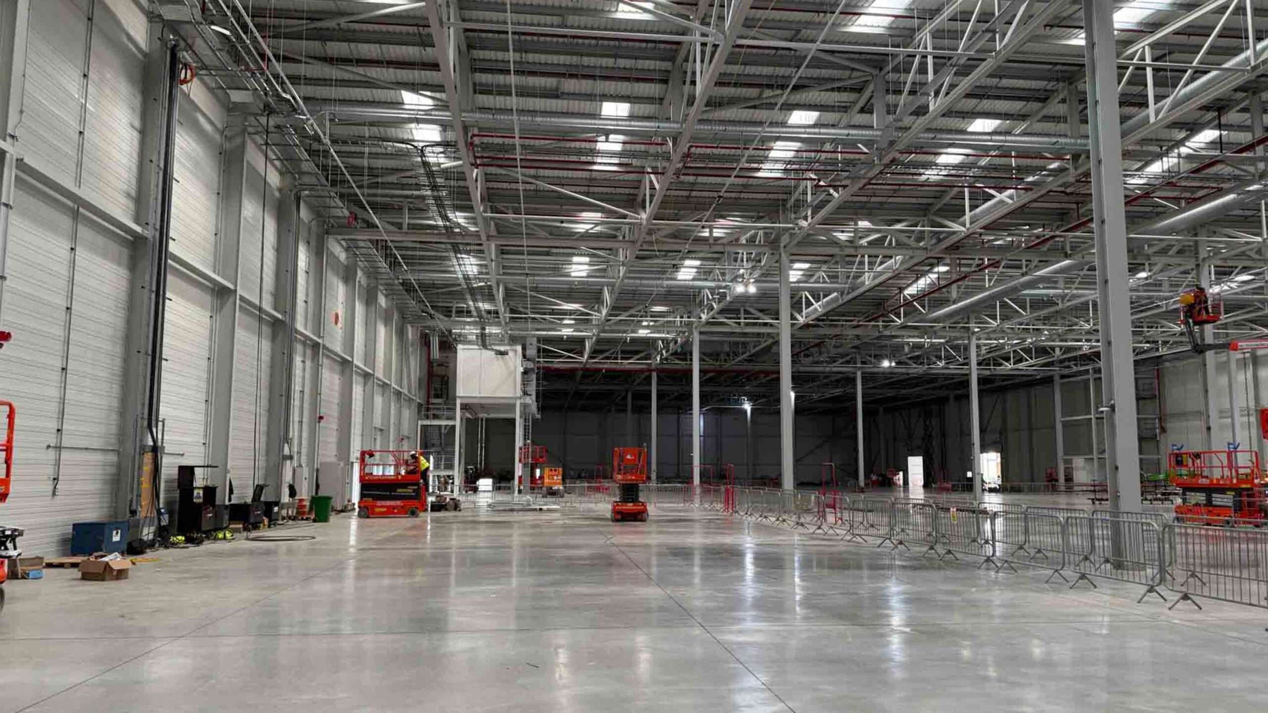 Industrial Warehouse Construction – Steel Framework and Interior Build | Natta Spacious industrial warehouse interior under construction with steel beams, high ceilings, and access equipment on site - BMW Mini Plant Oxford - Groundworks Package