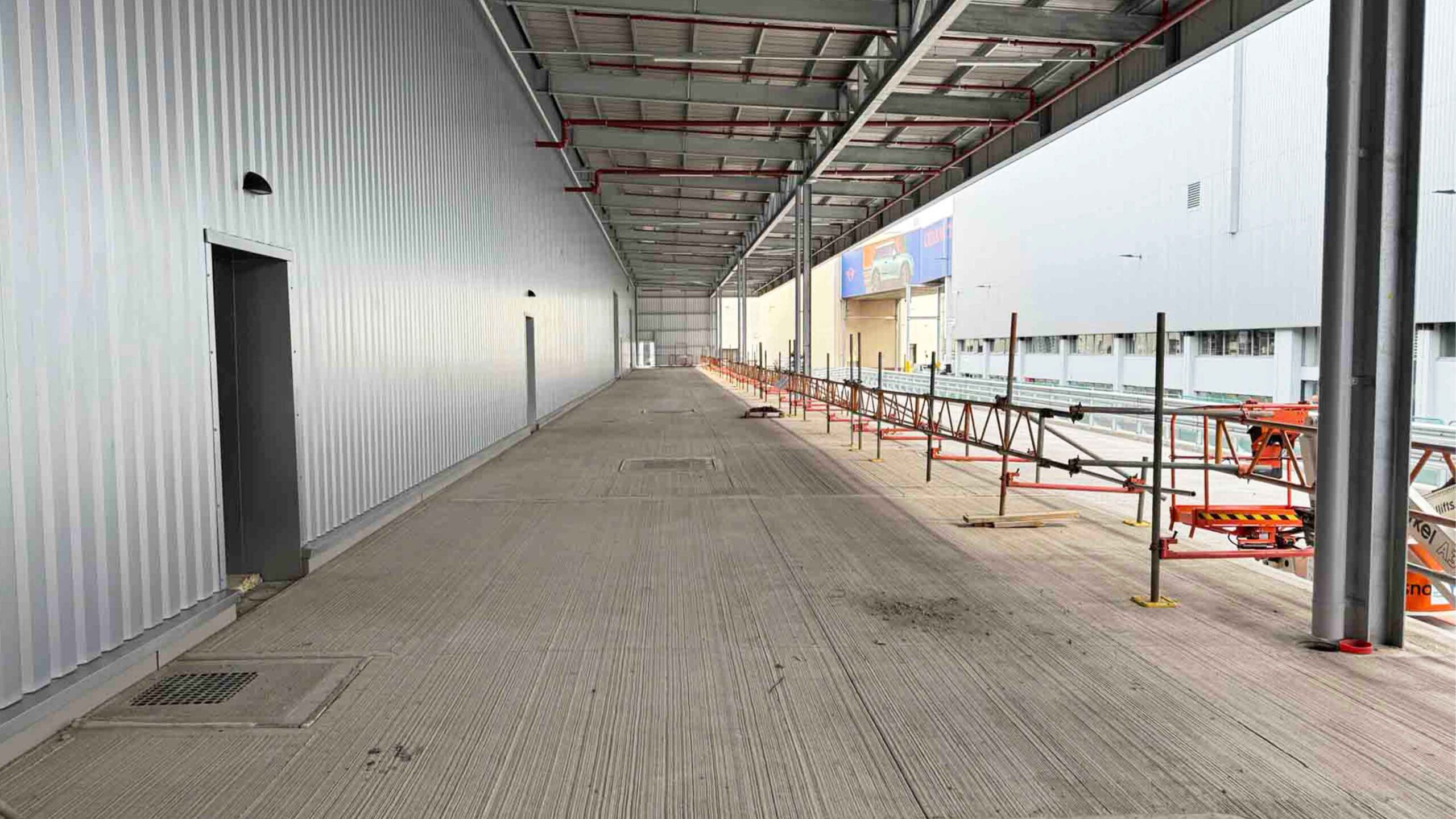 Warehouse Walkway Construction with Metal Cladding and Scaffolding | Natta Industrial warehouse walkway under construction with metal cladding, scaffolding, and overhead roof structure - BMW Mini Plant Oxford - Groundworks Package