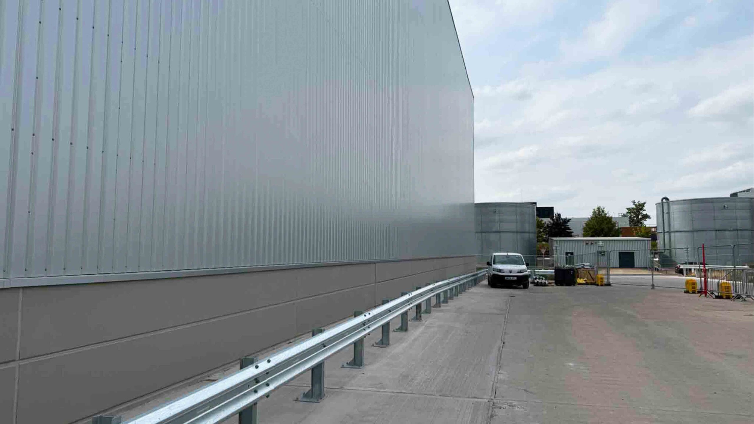 Industrial Warehouse Exterior with Metal Cladding and Safety Barriers | Natta Exterior view of industrial warehouse with metal cladding, safety barriers, and storage tanks on a commercial -BMW Mini Plant Oxford - Groundworks Package