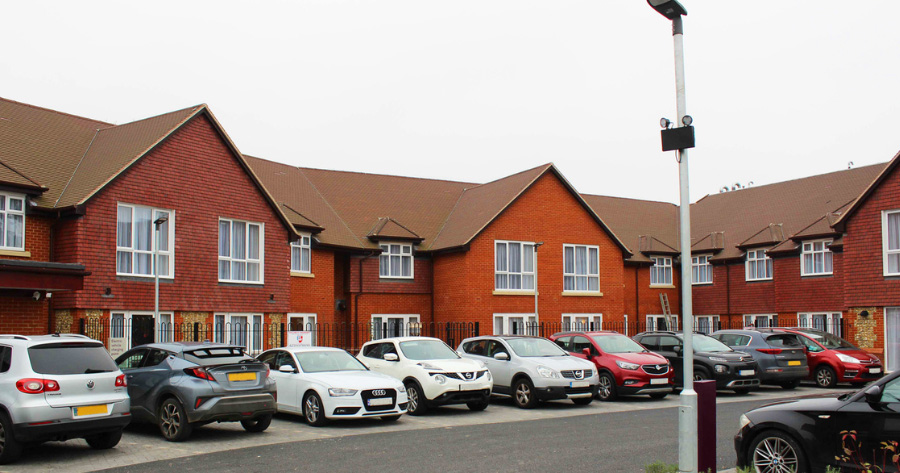 Row of red brick townhouses with cars parked along the street in front of them, daytime. PR