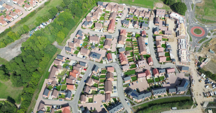Aerial view of a residential neighborhood with tightly packed houses, clay roofs, and green lawns along winding streets.