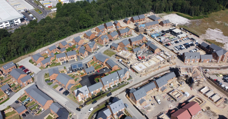 Aerial view of a developing suburban housing neighborhood with rows of new brick townhouses and a construction site nearby.